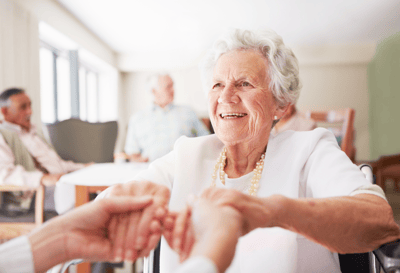 Smiling elderly woman with caregivers in a common area.