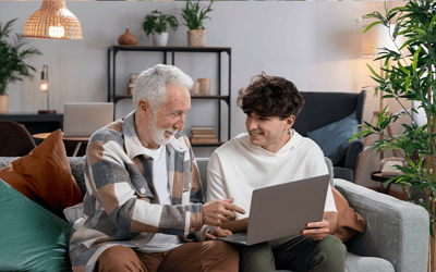 Elderly man and young man with a laptop in a cozy living room.