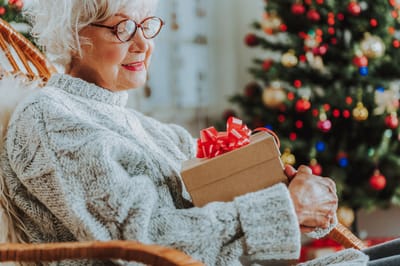 Senior woman with a gift by a Christmas tree