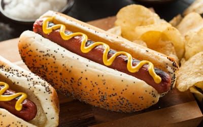 Hot dog with mustard and potato chips on a wooden board.