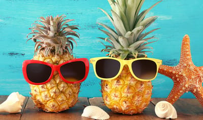 Two pineapples wearing sunglasses on a table.