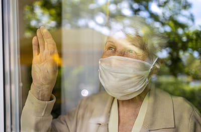 Older woman waving from behind a window