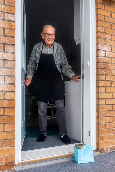 A smiling senior man at the door, wearing an apron