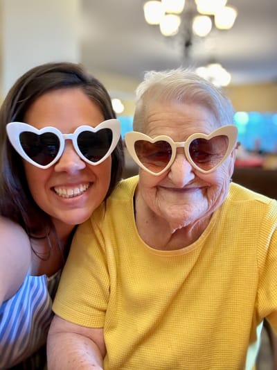 Two women in heart-shaped sunglasses smiling together