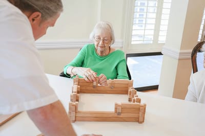 Resident engaging in a group activity with staff assistance