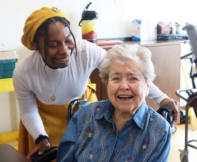 A smiling resident with staff member in a facility interior