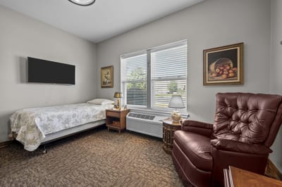 A cozy private resident room with a bed and recliner