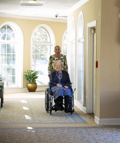 Resident in a wheelchair with staff member in hallway
