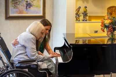A resident and staff member playing piano together