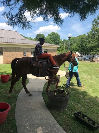 Resident riding a horse with staff assistance outside