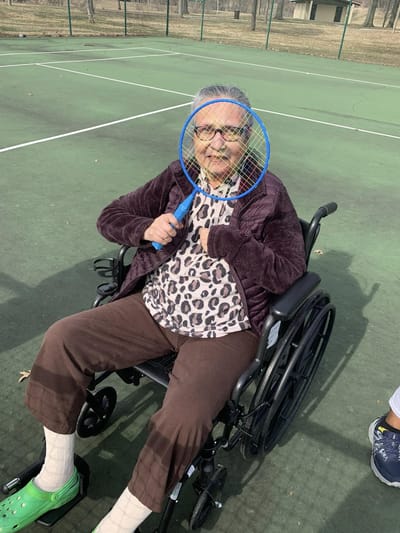 Resident in a wheelchair holding a tennis racket on a court