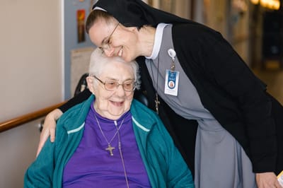 A resident smiling with a staff member in a hallway