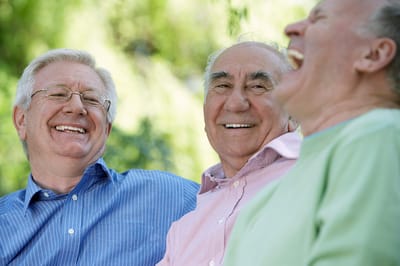 Three elderly men laughing together outdoors