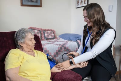 Staff member taking a resident's blood pressure in a cozy room