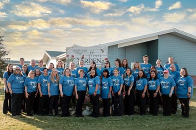 Staff and residents posing outside the Prairie Ridge Village sign