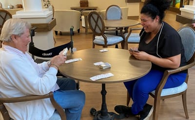 Resident and staff playing cards in the activity room