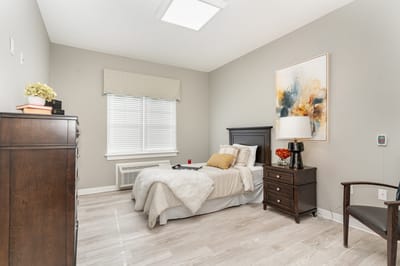 A neatly arranged private resident room with a bed and artwork