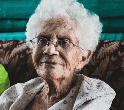 An elderly woman with glasses seated indoors