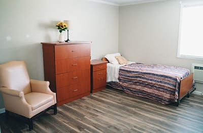 A well-furnished resident room with a bed and chair