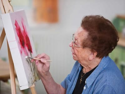 An elderly woman painting on canvas in an art room