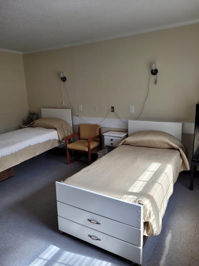 A shared resident room with two beds and a chair