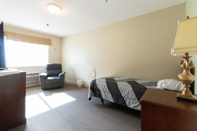 A private resident room with bed and chair