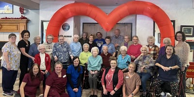 Residents and staff celebrating in a common area with a heart-shaped decoration