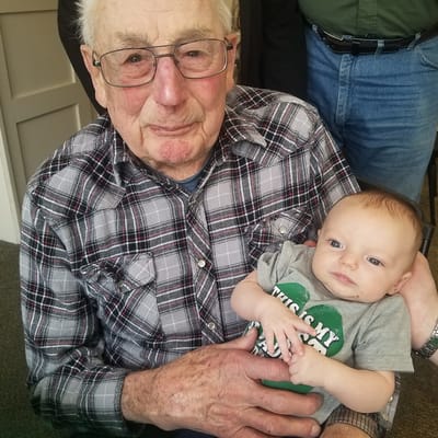 An elderly man holding a baby, both smiling