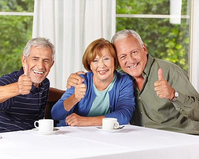 Three seniors enjoying tea and giving thumbs up.