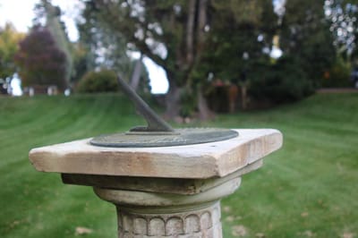 Sundial on a stone pedestal in a grassy area