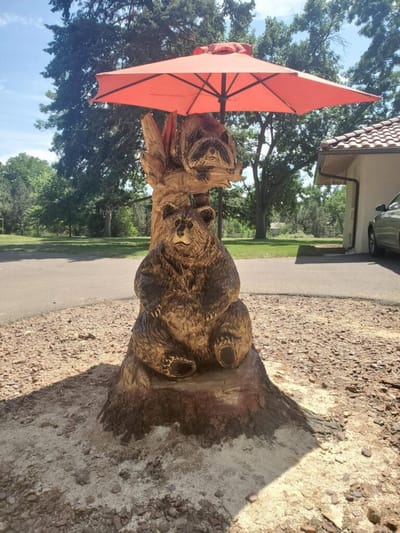 Wooden bear sculpture with an umbrella in outdoor space.