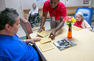 Residents playing bingo with staff in a common area.