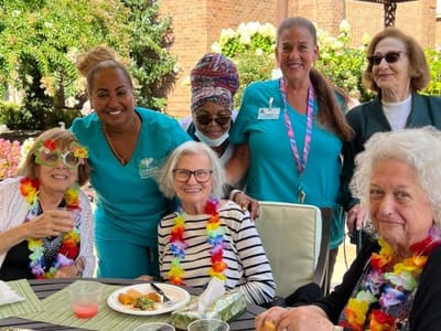 Residents and staff celebrate outdoors with leis and food.