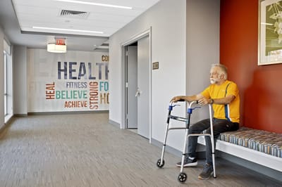 Resident sitting in a corridor near wellness-themed wall art.