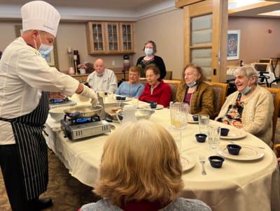 Residents enjoying a cooking demonstration at a dining table.