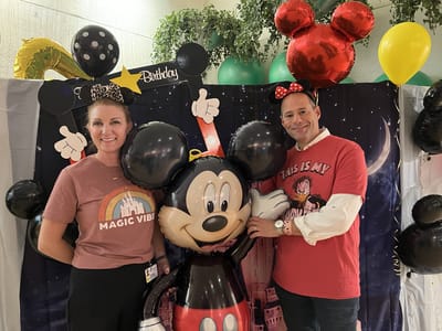 Staff celebrating a birthday event with decorations and costumes.