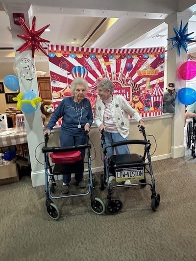 Two residents with walkers in a festive interior.