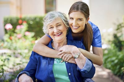 Caregiver and resident smiling in a garden.