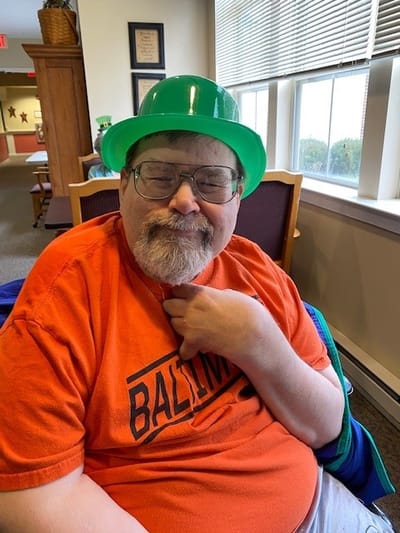 Resident wearing a green hat, smiling indoors.