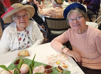 Two smiling residents enjoying tea and pastries.