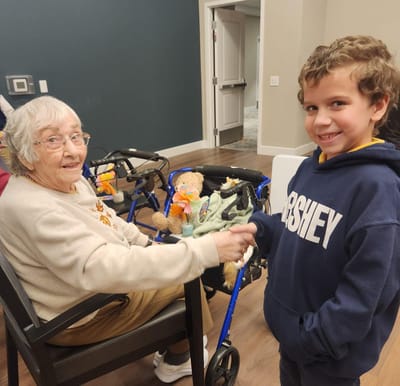 Elderly woman and young boy shaking hands in common area.