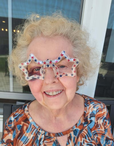 Elderly woman wearing star-shaped sunglasses with a smile.