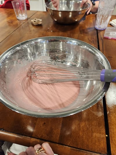 Bowl of pink mixture with whisk on a table