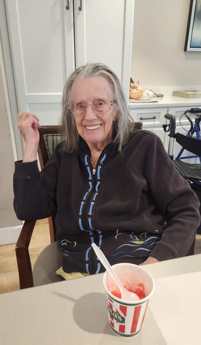 Smiling elderly woman with dessert in a dining area.