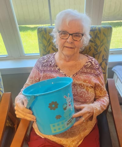 Senior resident holding a colorful bucket in a bright room.