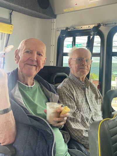 Two elderly men on a bus, smiling.