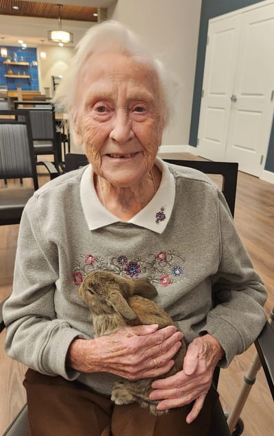 Elderly woman holding a rabbit, smiling.