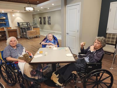 Three elderly women sitting around a table with snacks.