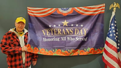 Resident posing with Veterans Day banner indoors.