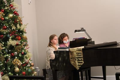 Two women playing piano near a Christmas tree.